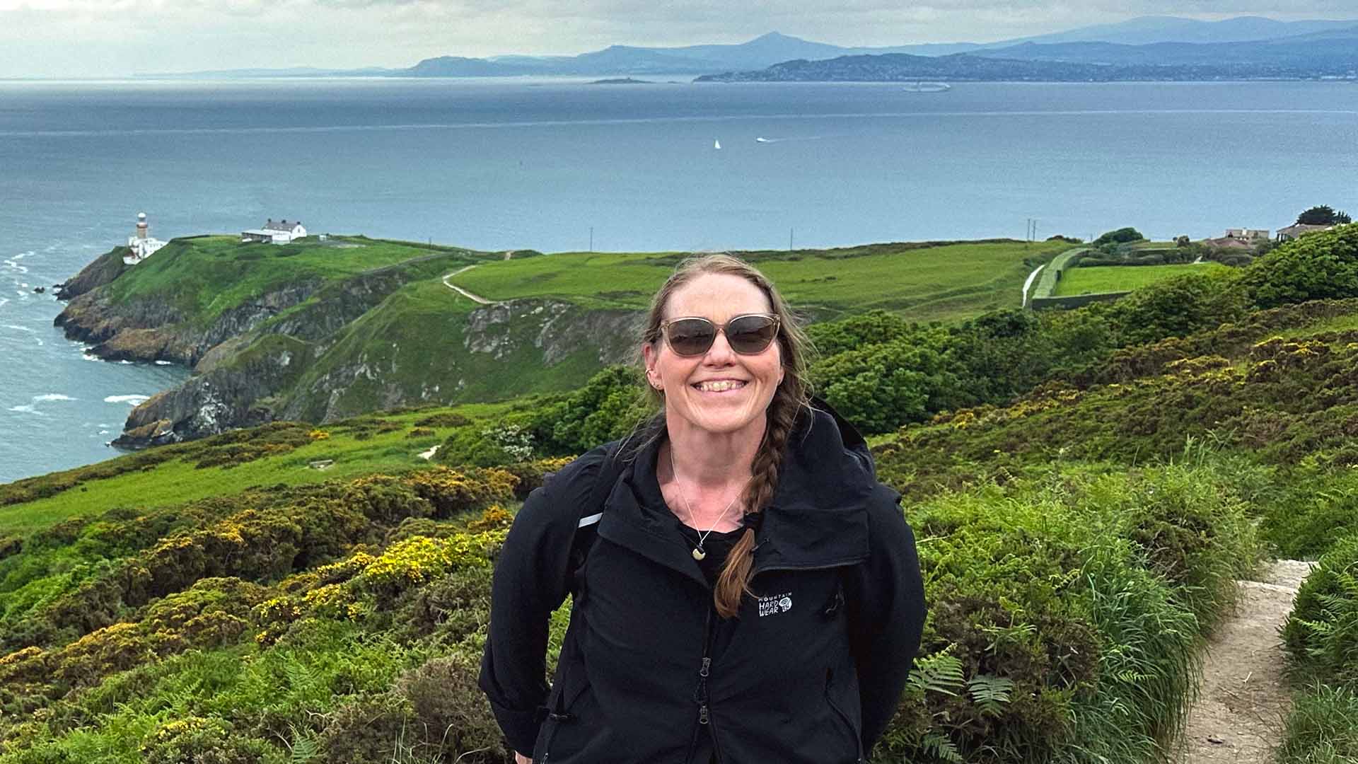 Debra standing in front the ocean with large greenery behind